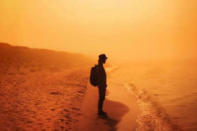 黑夹克男子站在布朗砂在日落
